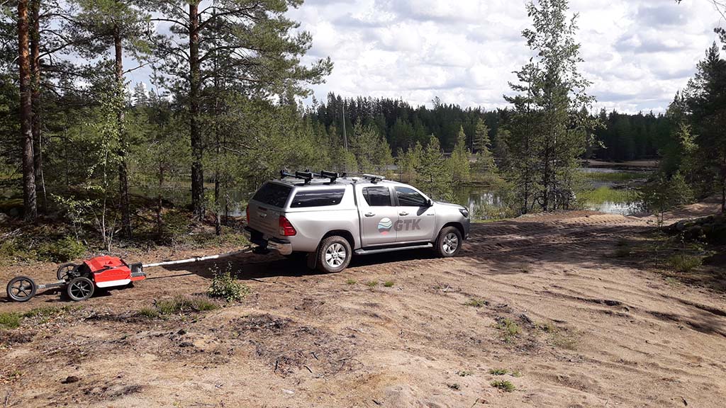 Auto metsäisessä maastossa, mukana perässä vedettävä mittalaite.